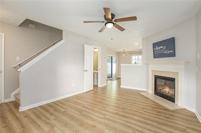 unfurnished living room featuring a fireplace, a ceiling fan, baseboards, stairway, and light wood finished floors