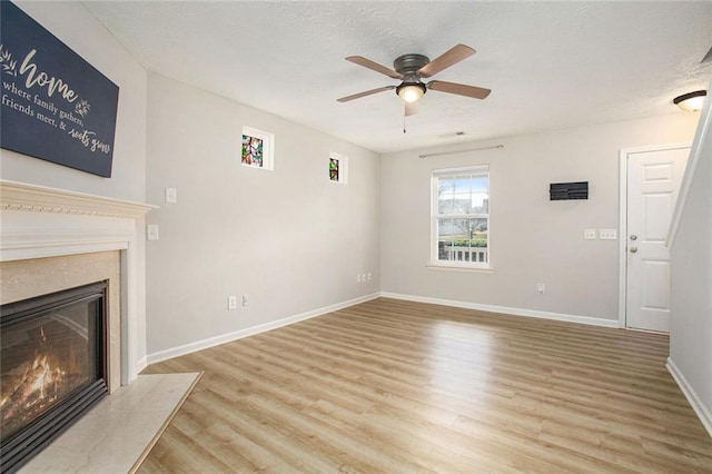 unfurnished living room with ceiling fan, light wood-style flooring, baseboards, and a premium fireplace