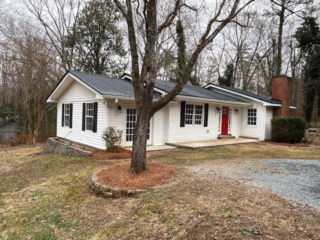 ranch-style house with gravel driveway, metal roof, and a front lawn