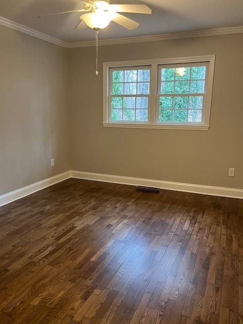 empty room featuring dark wood-type flooring, a wealth of natural light, crown molding, and baseboards