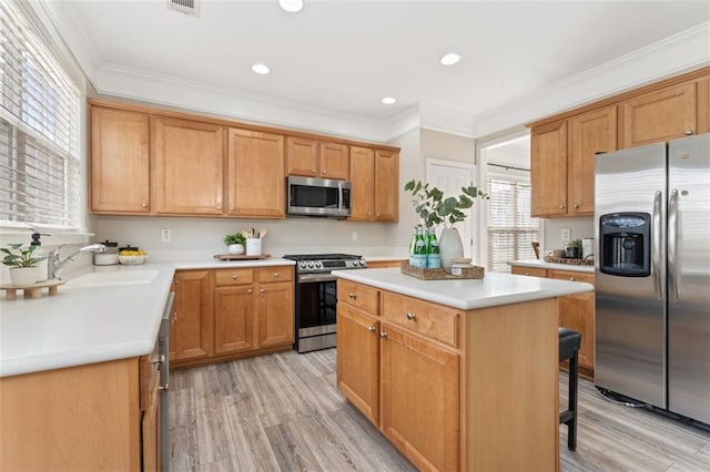 kitchen featuring a center island, crown molding, light countertops, stainless steel appliances, and a sink