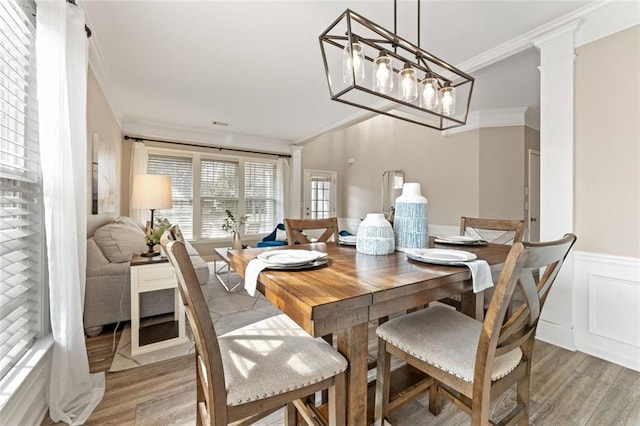 dining room with crown molding, a decorative wall, light wood finished floors, and wainscoting