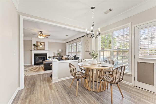 dining space featuring light wood-type flooring, visible vents, a glass covered fireplace, and ornamental molding