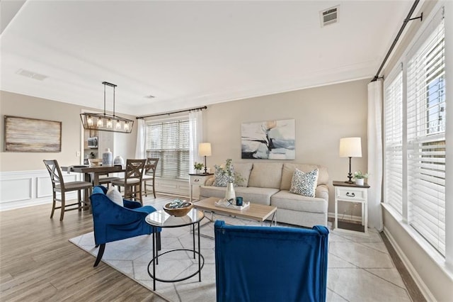 living area featuring visible vents, light wood-style flooring, a decorative wall, and ornamental molding