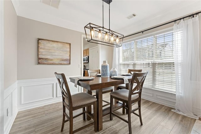 dining room featuring light wood finished floors, visible vents, a decorative wall, and an inviting chandelier