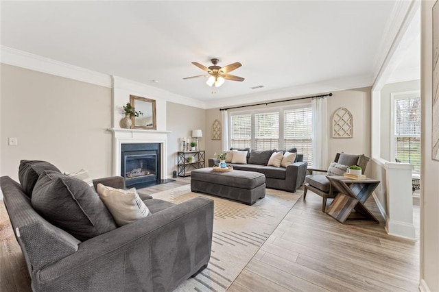 living room featuring a fireplace with flush hearth, light wood-style flooring, a ceiling fan, and crown molding