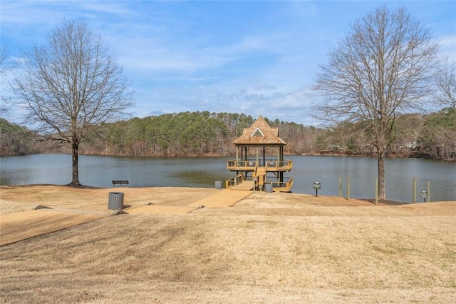 view of dock with a lawn, a forest view, and a water view