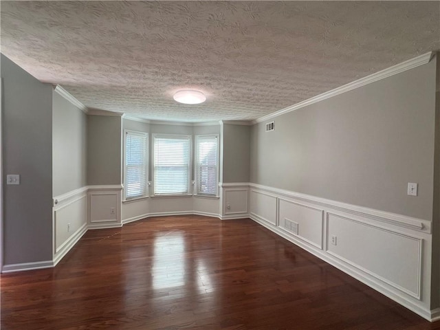 empty room with a textured ceiling, ornamental molding, wood finished floors, and visible vents