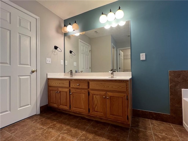 bathroom featuring a tub to relax in, a sink, baseboards, tile patterned floors, and double vanity