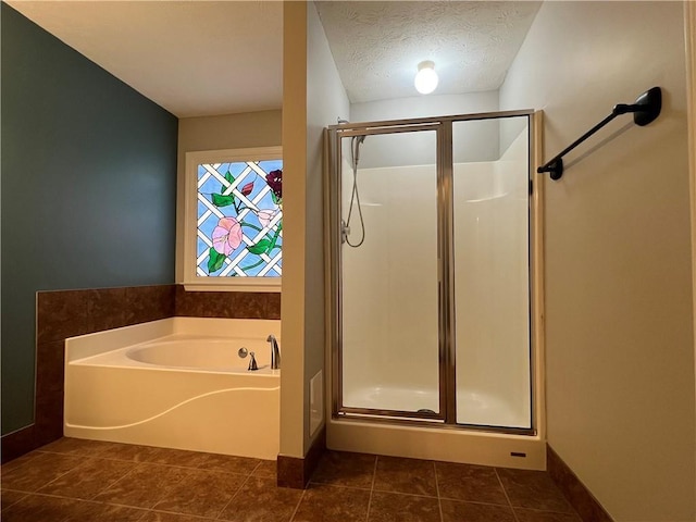 bathroom featuring a stall shower, a textured ceiling, tile patterned flooring, baseboards, and a bath