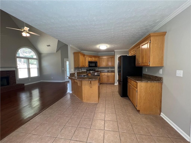 kitchen with light tile patterned floors, open floor plan, a sink, a peninsula, and black appliances