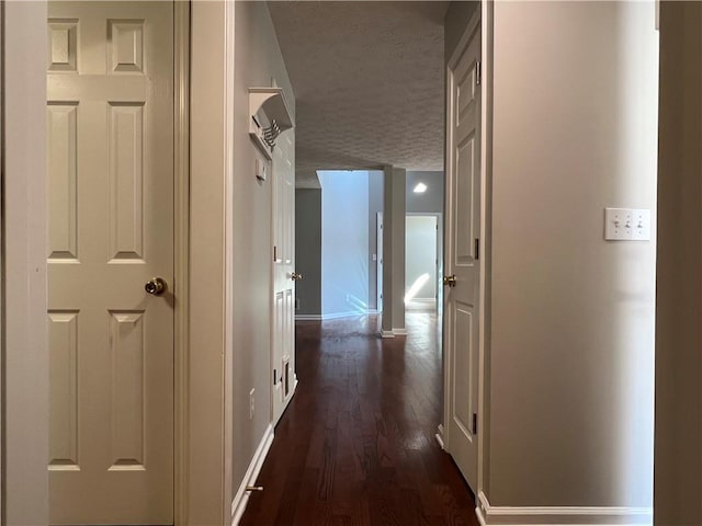 corridor with a textured ceiling, dark wood finished floors, and baseboards