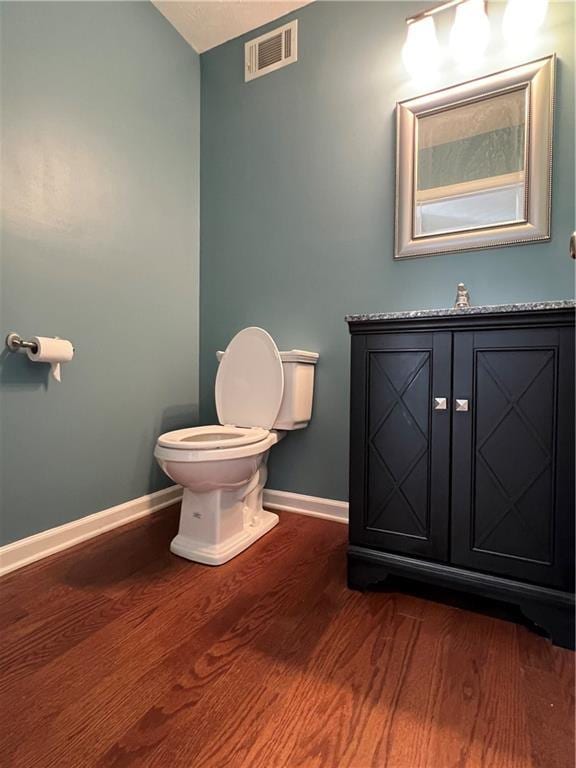 half bathroom with toilet, baseboards, visible vents, and wood finished floors