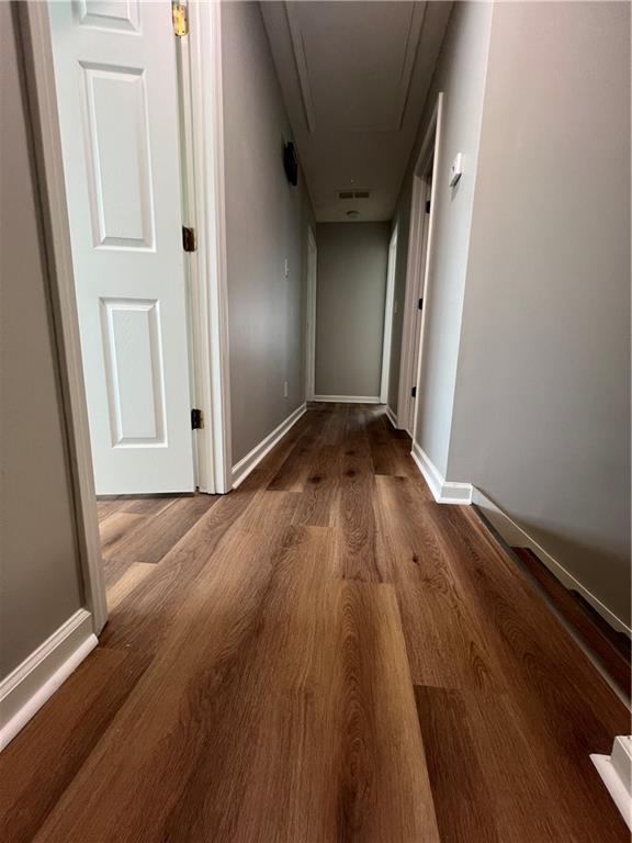 hall featuring attic access, visible vents, baseboards, and wood finished floors