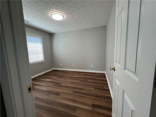 unfurnished bedroom featuring a textured ceiling, dark wood finished floors, and baseboards