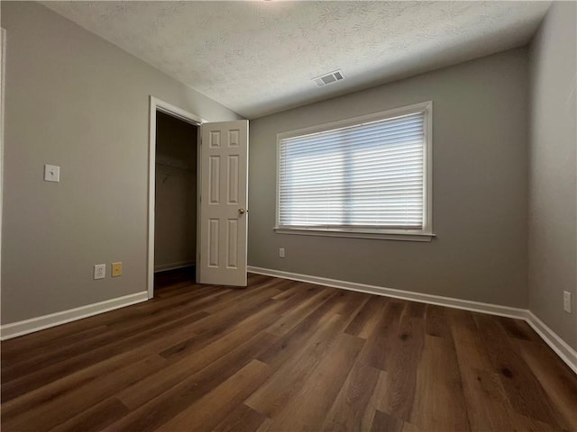 unfurnished bedroom featuring dark wood-style flooring, visible vents, a textured ceiling, and baseboards