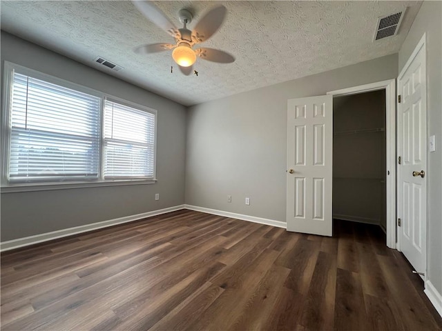 unfurnished bedroom with dark wood-style flooring, visible vents, a textured ceiling, and baseboards