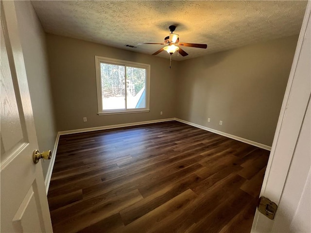 empty room with dark wood finished floors, visible vents, a ceiling fan, a textured ceiling, and baseboards