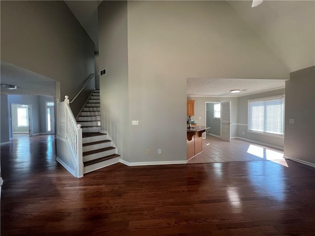 foyer featuring high vaulted ceiling, wood finished floors, visible vents, baseboards, and stairway