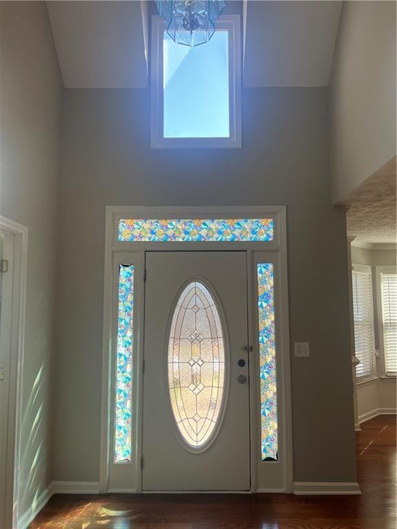 foyer entrance with high vaulted ceiling, baseboards, and wood finished floors