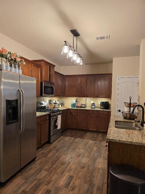 kitchen with light stone counters, sink, dark hardwood / wood-style flooring, pendant lighting, and appliances with stainless steel finishes