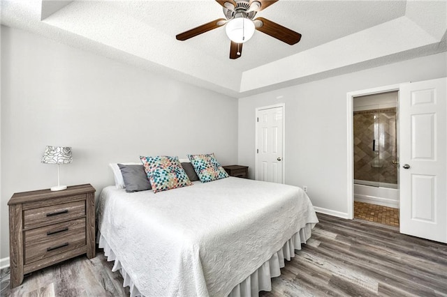 bedroom with connected bathroom, a raised ceiling, baseboards, and wood finished floors