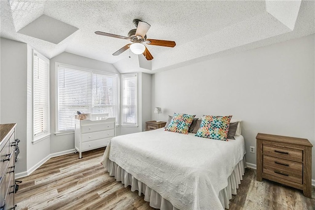 bedroom with a raised ceiling, wood finished floors, baseboards, and a textured ceiling