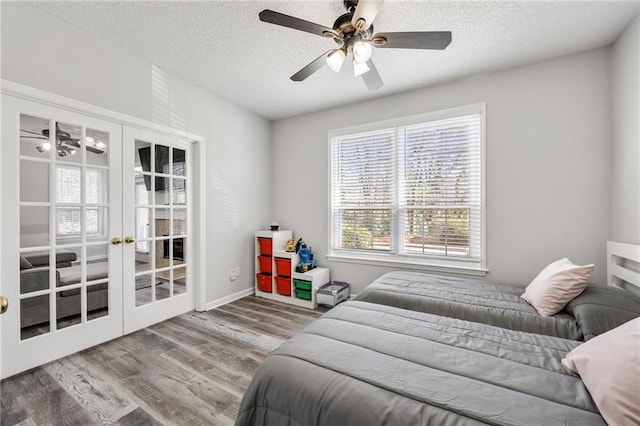 bedroom with a textured ceiling, wood finished floors, french doors, baseboards, and ceiling fan