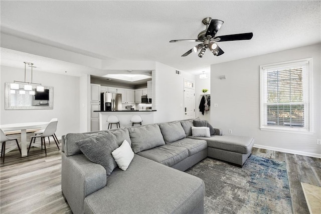 living room featuring light wood-style flooring, a textured ceiling, baseboards, and ceiling fan