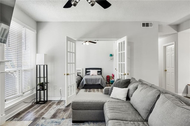 living area with a ceiling fan, wood finished floors, visible vents, and french doors