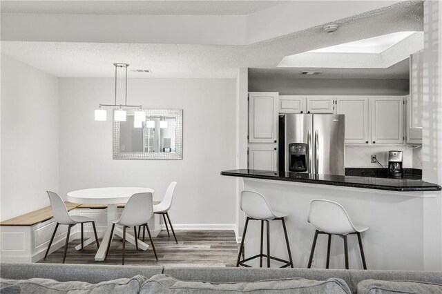 kitchen with a textured ceiling, dark countertops, white cabinetry, stainless steel fridge, and a peninsula