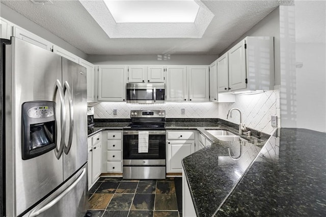 kitchen with a sink, stone finish flooring, tasteful backsplash, stainless steel appliances, and white cabinets