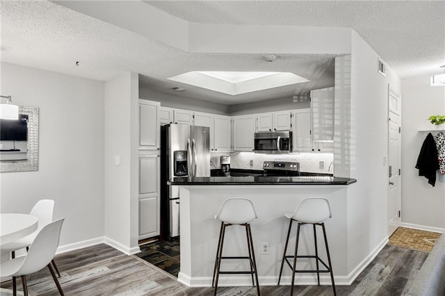 kitchen with visible vents, a peninsula, dark wood-type flooring, appliances with stainless steel finishes, and dark countertops