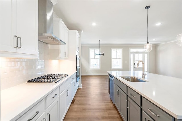 kitchen with wall chimney range hood, sink, hanging light fixtures, appliances with stainless steel finishes, and white cabinetry