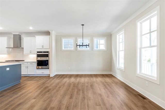 kitchen featuring white cabinets, wall chimney range hood, decorative light fixtures, stovetop, and stainless steel double oven