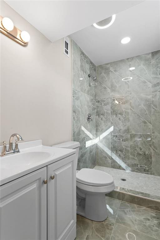 bathroom featuring a tile shower, vanity, and toilet