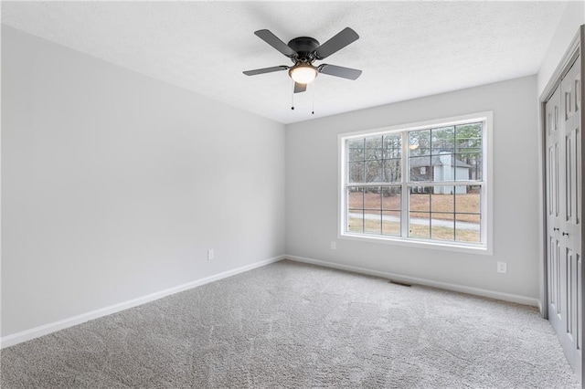 carpeted spare room featuring a ceiling fan, visible vents, a textured ceiling, and baseboards