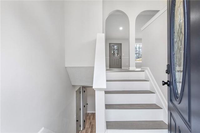 stairway featuring baseboards, arched walkways, and wood finished floors