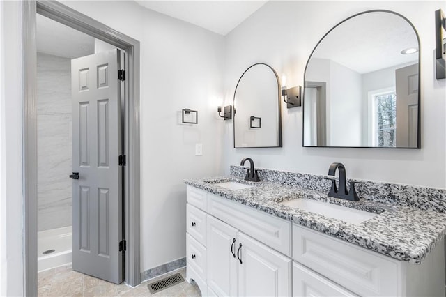 bathroom with double vanity, a stall shower, baseboards, and a sink