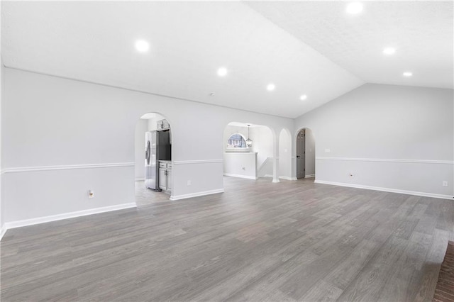 unfurnished living room with arched walkways, baseboards, wood finished floors, and lofted ceiling