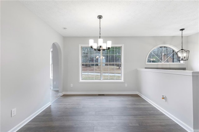 unfurnished dining area with a chandelier, arched walkways, a textured ceiling, baseboards, and dark wood-style floors