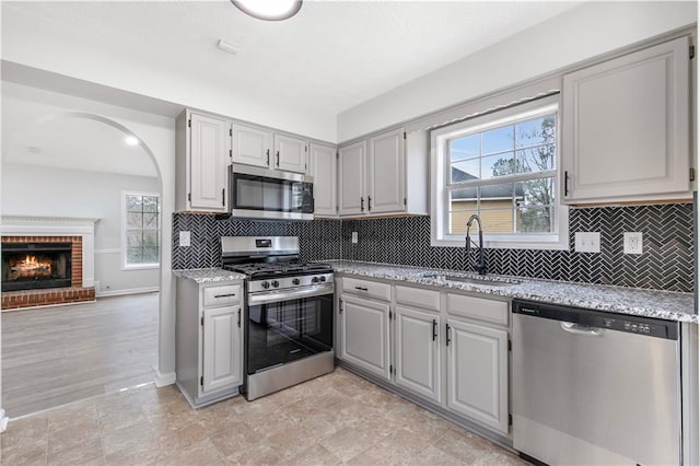 kitchen with light stone counters, a fireplace, backsplash, appliances with stainless steel finishes, and a sink