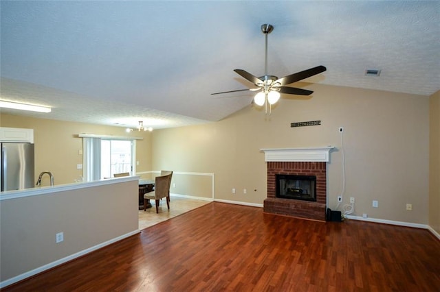 unfurnished living room with a textured ceiling, dark hardwood / wood-style flooring, a brick fireplace, lofted ceiling, and ceiling fan with notable chandelier