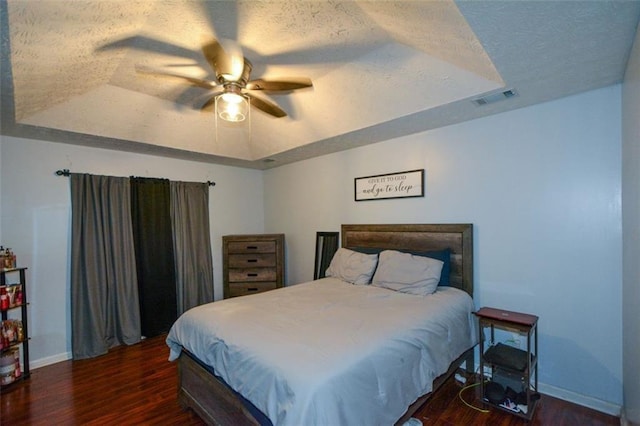 bedroom with dark hardwood / wood-style flooring, ceiling fan, and a raised ceiling