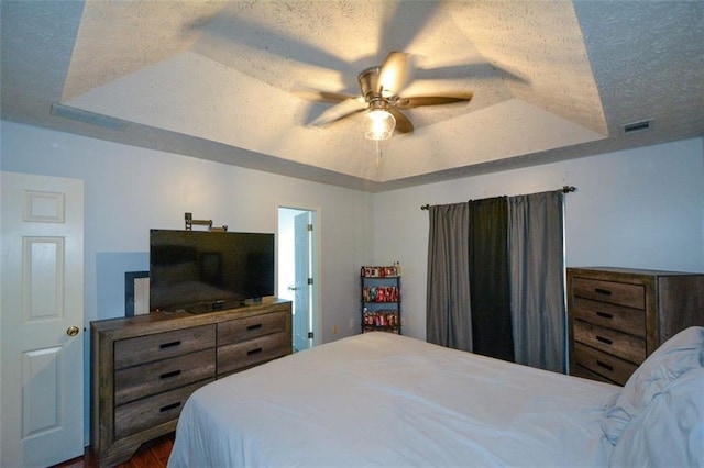 bedroom featuring a textured ceiling, wood-type flooring, ceiling fan, and a tray ceiling