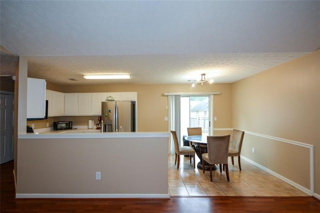 kitchen featuring light hardwood / wood-style floors, white cabinets, kitchen peninsula, a textured ceiling, and stainless steel fridge with ice dispenser