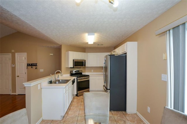 kitchen with stainless steel appliances, sink, kitchen peninsula, lofted ceiling, and white cabinets