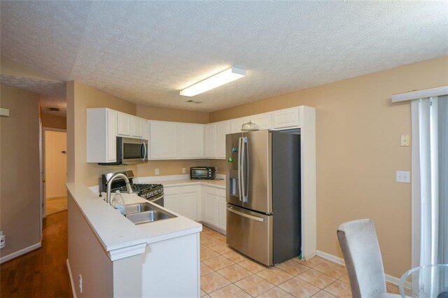 kitchen with appliances with stainless steel finishes, a textured ceiling, sink, white cabinets, and kitchen peninsula