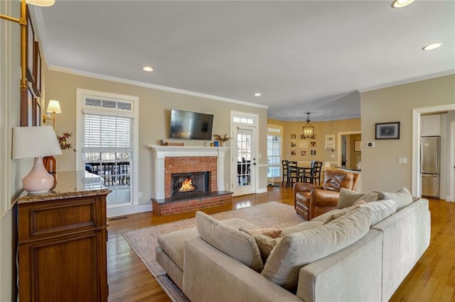 living room with light wood-type flooring, a brick fireplace, plenty of natural light, and ornamental molding