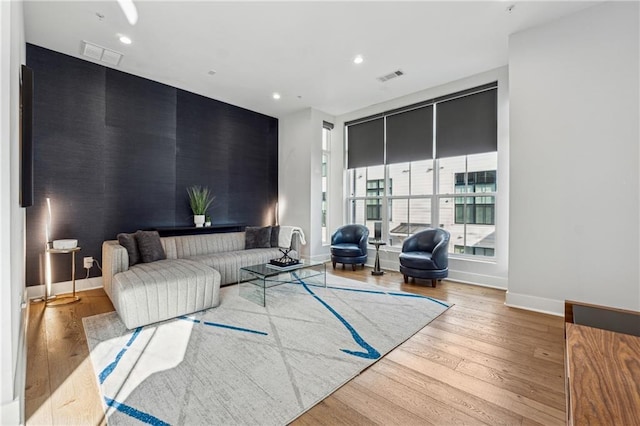 living area with light wood-style floors, baseboards, an accent wall, and visible vents